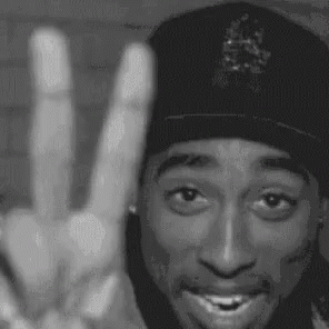 A Black And White Photo Of A Man Wearing A Hat Giving A Peace Sign . GIF