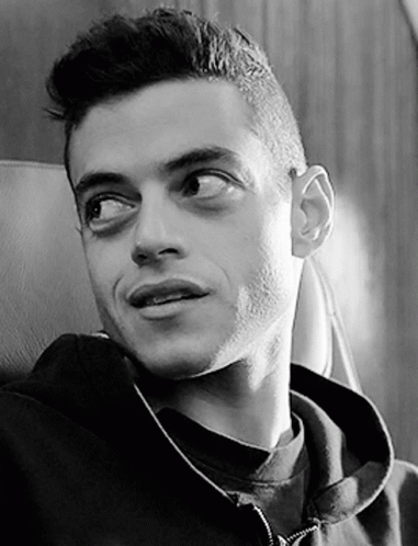 A Black And White Photo Of A Man Wearing A Hoodie Sitting In A Chair . GIF