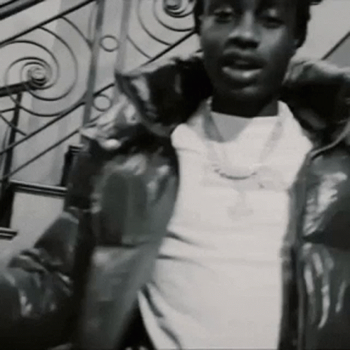 A Black And White Photo Of A Man Wearing A Jacket And A Necklace . GIF