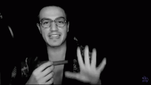 A Black And White Photo Of A Man Wearing Glasses Holding Something In His Hand . GIF