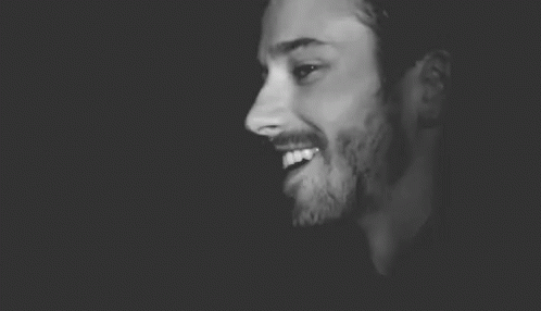 a black and white photo of a man with a beard wearing a hat and smiling .