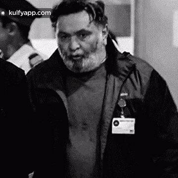 A Black And White Photo Of A Man With A Beard Wearing A Jacket And A Badge . GIF