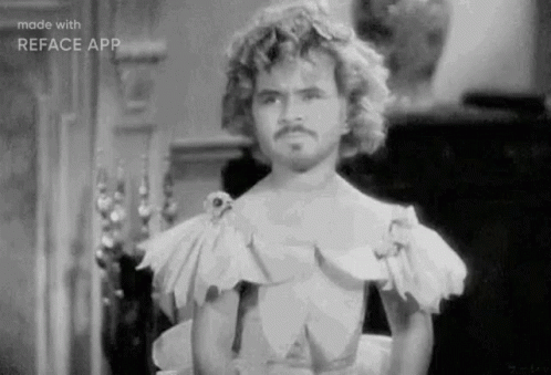 A Black And White Photo Of A Man With Curly Hair And A Mustache Wearing A Dress . GIF