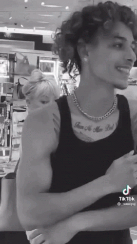 A Black And White Photo Of A Man With Curly Hair And A Tattoo On His Chest GIF