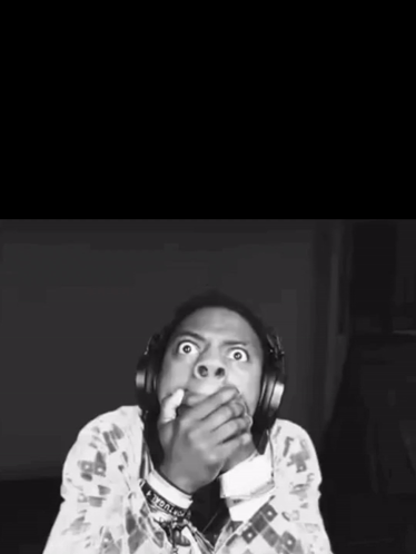 A Black And White Photo Of A Man With Headphones Covering His Mouth With His Hands GIF