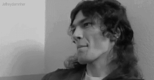 A Black And White Photo Of A Man With Long Curly Hair . GIF