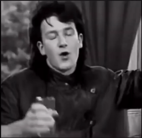 a black and white photo of a man with long hair singing into a microphone