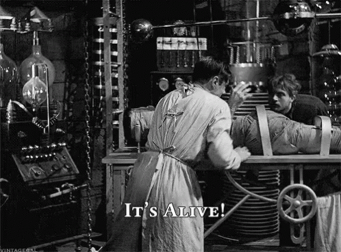 A Black And White Photo Of A Man Working On A Mummy With The Words It 'S Alive Below Him GIF