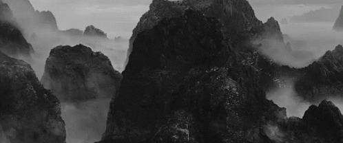 A Black And White Photo Of A Mountain Covered In Fog GIF