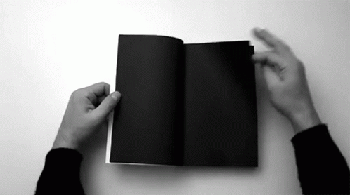 A Black And White Photo Of A Person Holding A Black Book Open . GIF