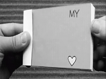 A Black And White Photo Of A Person Holding A Piece Of Paper With The Word `` My '' And A Heart Drawn On It . GIF