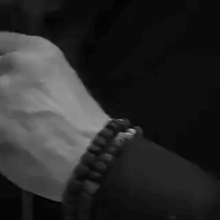 A Black And White Photo Of A Person Holding Another Person 'S Hand While Wearing A Bracelet . GIF