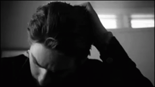 A Black And White Photo Of A Person Holding Their Head . GIF
