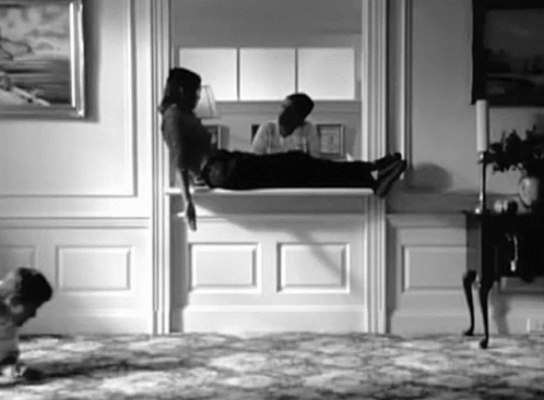 A Black And White Photo Of A Person Laying On A Mantle In A Living Room . GIF