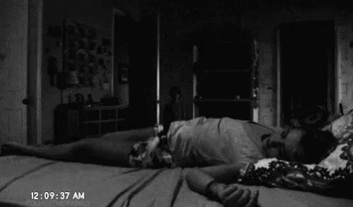 A Black And White Photo Of A Person Laying On Their Back On A Bed In A Dark Room . GIF