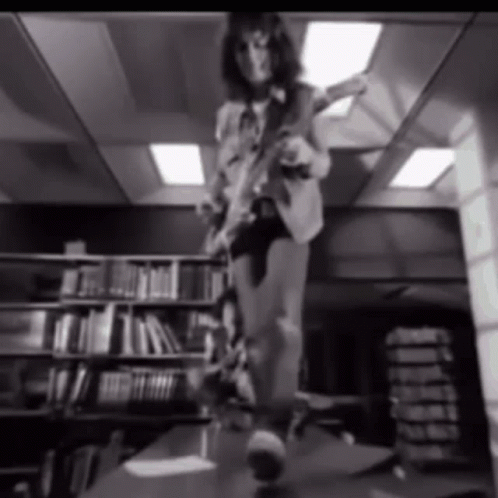 A Black And White Photo Of A Person Playing A Guitar In A Library GIF