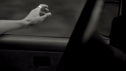 a black and white photo of a person 's hand reaching out from a car window