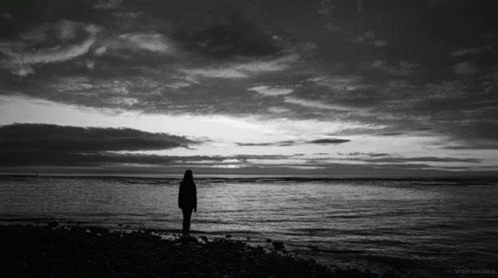 A Black And White Photo Of A Person Standing In Front Of A Body Of Water GIF