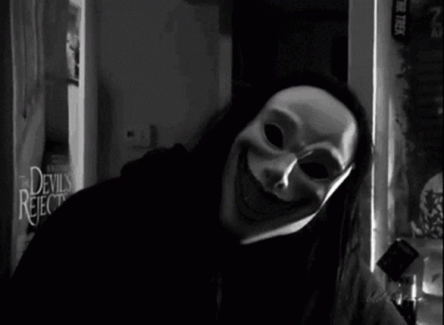 A Black And White Photo Of A Person Wearing A Mask In Front Of A Devils Rejects Sign GIF