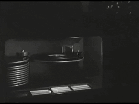 A Black And White Photo Of A Record Player And A Stack Of Records GIF