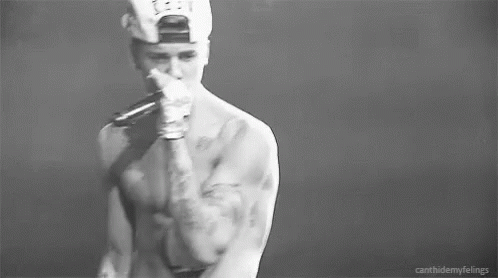 A Black And White Photo Of A Shirtless Man In A Baseball Cap Holding His Chest . GIF