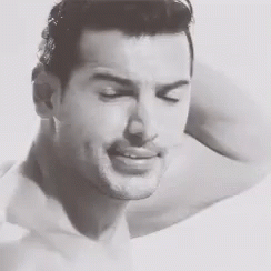A Black And White Photo Of A Shirtless Man Smiling With His Arm Behind His Head . GIF