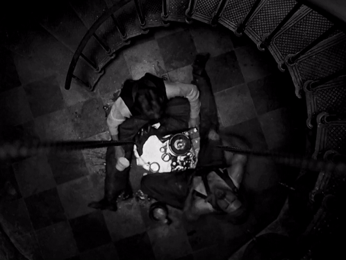 A Black And White Photo Of A Spiral Staircase With Two People Laying On The Floor GIF