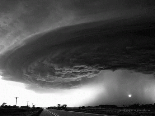 A Black And White Photo Of A Storm Over A Country Road GIF