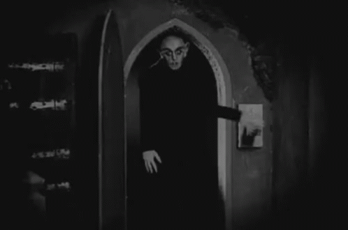 a black and white photo of a vampire standing in an archway .
