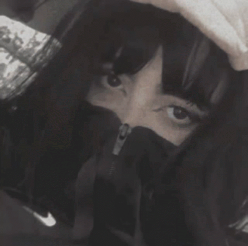 A Black And White Photo Of A Woman Covering Her Face With A Hood GIF