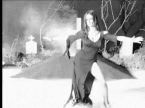 A Black And White Photo Of A Woman Dancing In A Cemetery . GIF