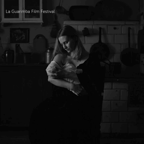 A Black And White Photo Of A Woman Holding A Baby With La Guarimba Film Festival In The Corner GIF