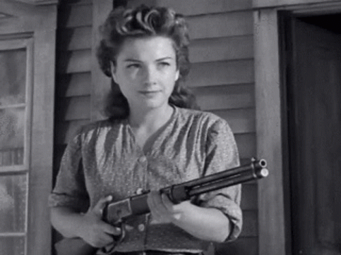 A Black And White Photo Of A Woman Holding A Shotgun . GIF