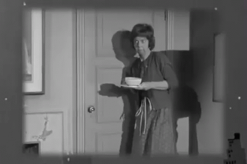 A Black And White Photo Of A Woman Holding A Tray With A Bowl On It GIF