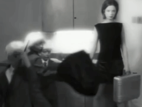 A Black And White Photo Of A Woman In A Black Dress Holding A Silver Briefcase GIF