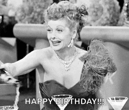 A Black And White Photo Of A Woman In A Dress Sitting At A Table With A Martini Glass And A Feather Boa . GIF