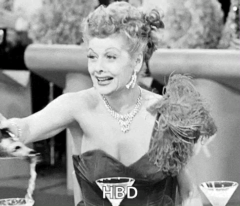 A Black And White Photo Of A Woman In A Dress Sitting At A Table With A Martini . GIF