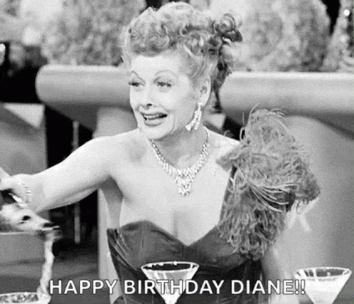 A Black And White Photo Of A Woman In A Dress Sitting At A Table With Two Martini Glasses And A Necklace . GIF
