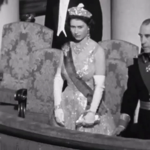 A Black And White Photo Of A Woman In A Dress Sitting In A Chair . GIF