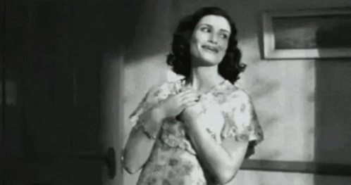 A Black And White Photo Of A Woman In A Floral Dress Standing In A Hallway . GIF