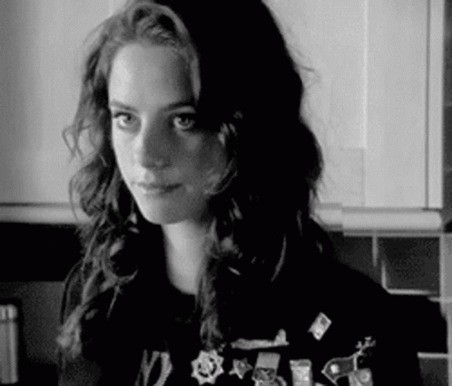 A Black And White Photo Of A Woman In A Kitchen Wearing A Sweater With Pins On It . GIF