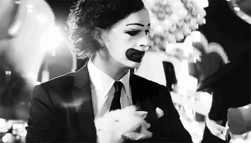 A Black And White Photo Of A Woman In A Suit And Tie With A Clown Makeup On Her Face . GIF