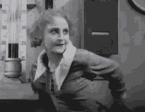 A Black And White Photo Of A Woman In A Suit Standing In Front Of A Thermometer . GIF