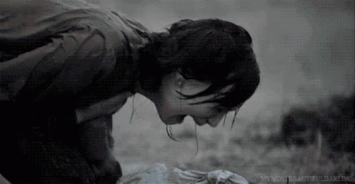 A Black And White Photo Of A Woman Kneeling Down With Her Head On A Dead Body . GIF