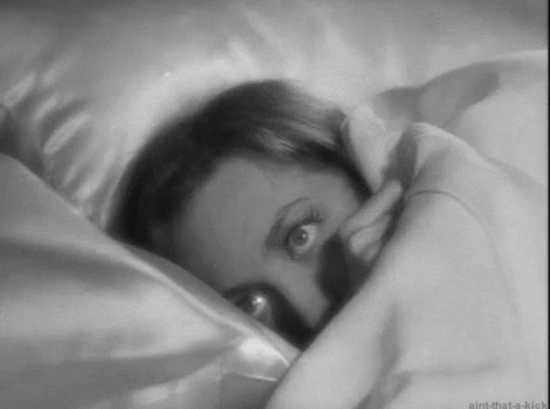 A Black And White Photo Of A Woman Laying In Bed With Her Eyes Open . GIF