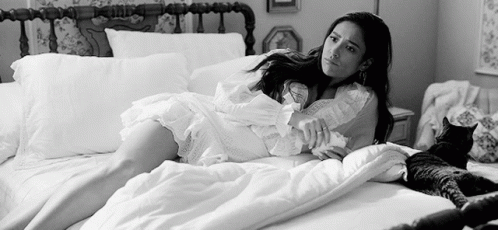 A Black And White Photo Of A Woman Laying On A Bed With A Cat . GIF