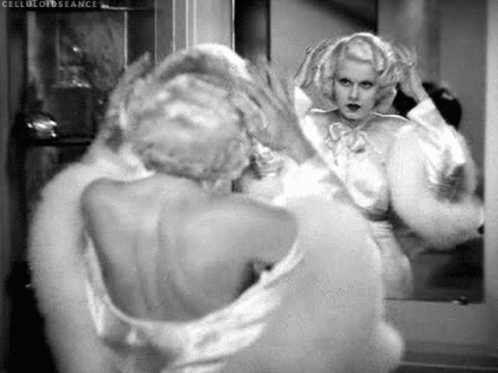 A Black And White Photo Of A Woman Looking At Herself In The Mirror . GIF