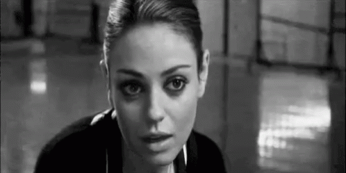 A Black And White Photo Of A Woman Looking At The Camera In A Room . GIF