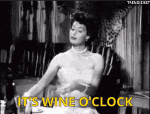 A Black And White Photo Of A Woman Sitting At A Table With The Words " It 'S Wine O ' Clock " GIF
