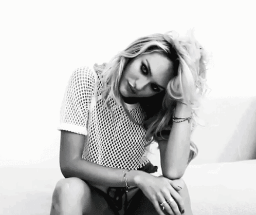 A Black And White Photo Of A Woman Sitting On A Couch Wearing A White Shirt . GIF
